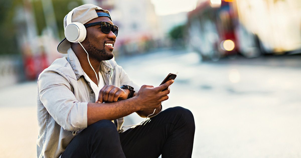 Close up of a young man sitting outdoors listening to music